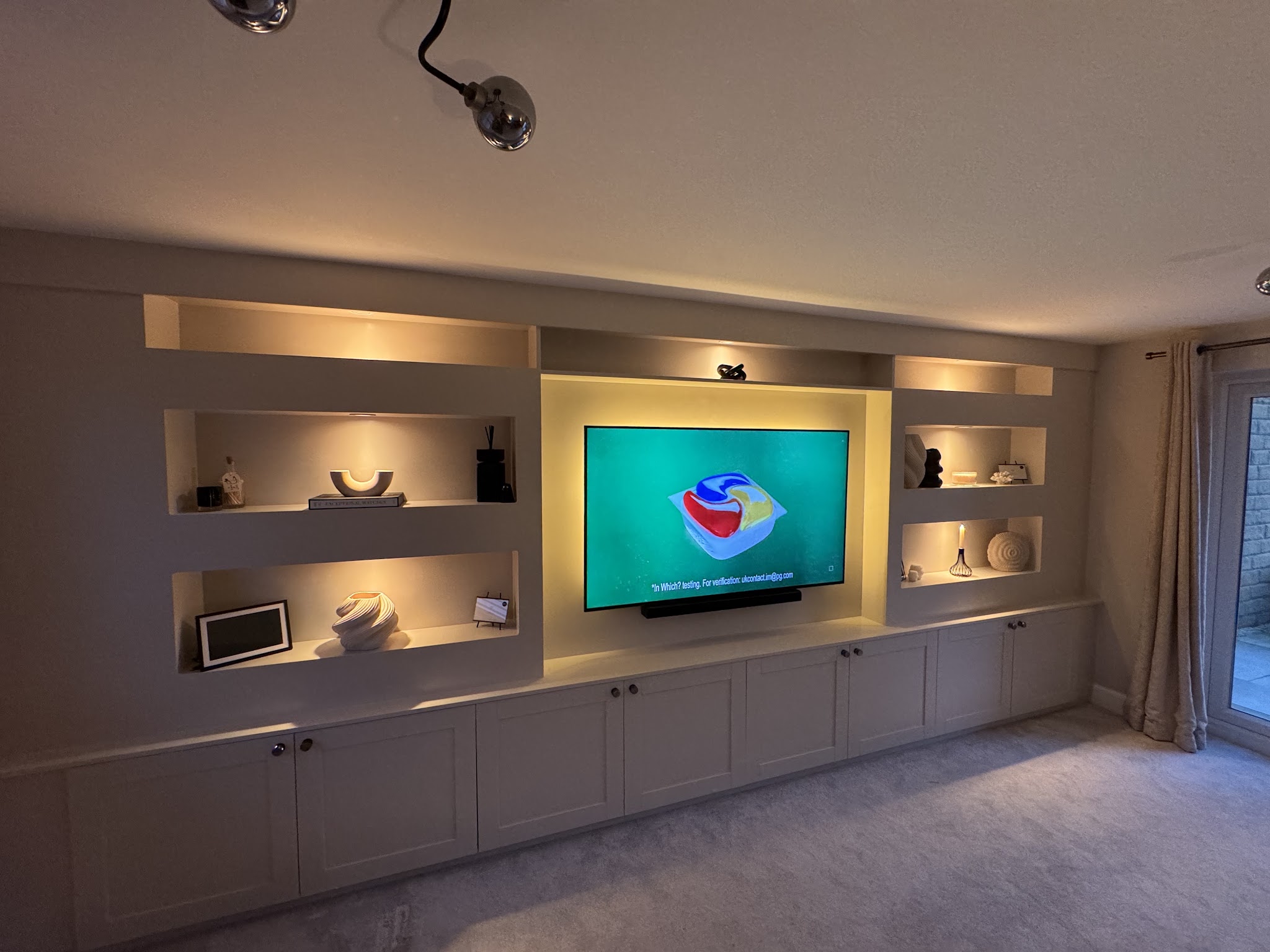 Finished media wall with painted shelving, cupboards and warm lighting